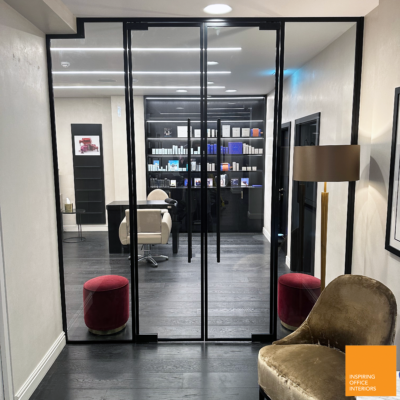 Frameless single glass partition doors opening onto a salon retail and treatment area.