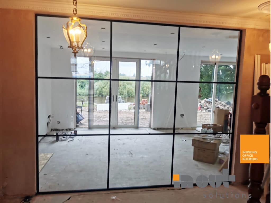 This glass room divider in York uses a black grid frame to section off the space, while clear glazing keeps the pendant lighting and outdoor view visible.
