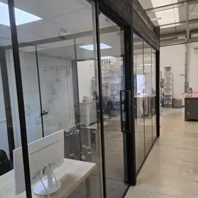 Black-framed glass partition in an industrial-style warehouse office, desk and monitor in foreground
