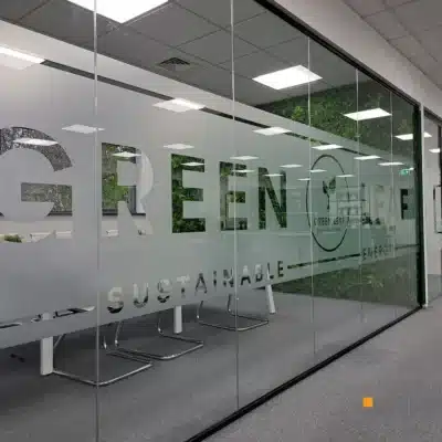 Frosted glass office partition with large "Green Leaf Sustainable Energy" branding overlooking a green wall at a Newcastle office