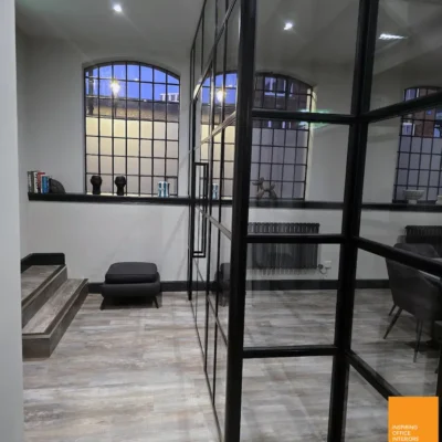 Black-framed glass partition dividing a lounge area in Birmingham period office with arched windows