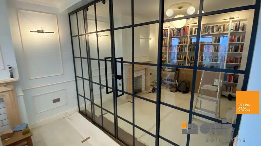 Black-framed glass walls and sliding glass doors enclosing a library room in London