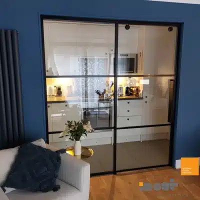 Black-framed interior sliding glass door dividing a blue kitchen from an adjoining room