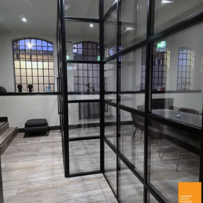 Angled black-framed glass partitions in Birmingham office breakout space with arched windows