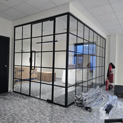 Corner view of a black framed glass partition enclosing an office pod with a hinged door