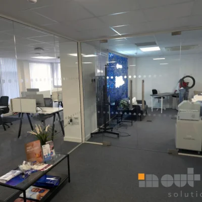 Frameless glass partition with dotted manifestation, dividing a reception area with desks and a decorative blue feature panel