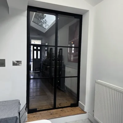 Black-framed double glass doors leading into a hallway with original front door visible beyond