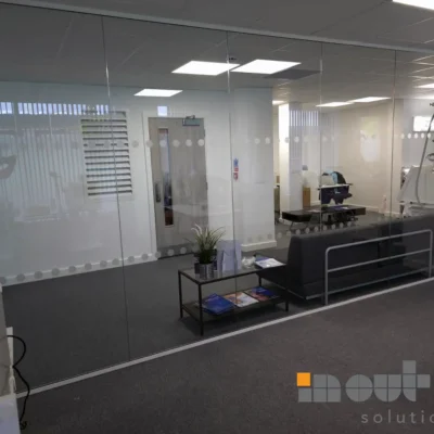 Frameless glass partition with dotted manifestation, waiting area with sofa and coffee table visible through the glass